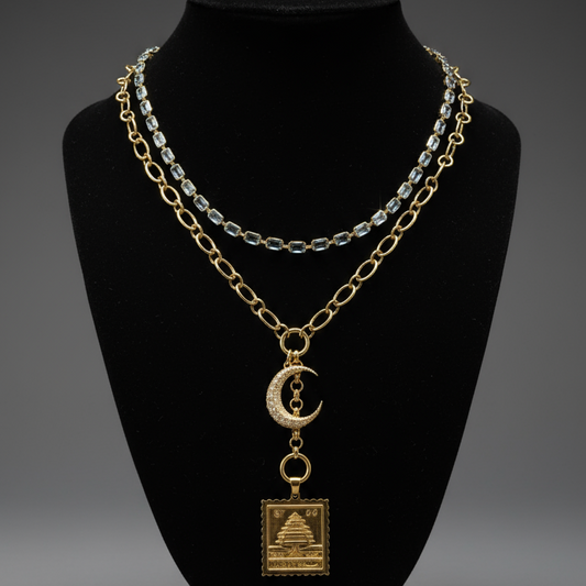 Solid gold crescent moon pendant layered with solid gold necklaces on a black display, handcrafted by SOIL Jewelry